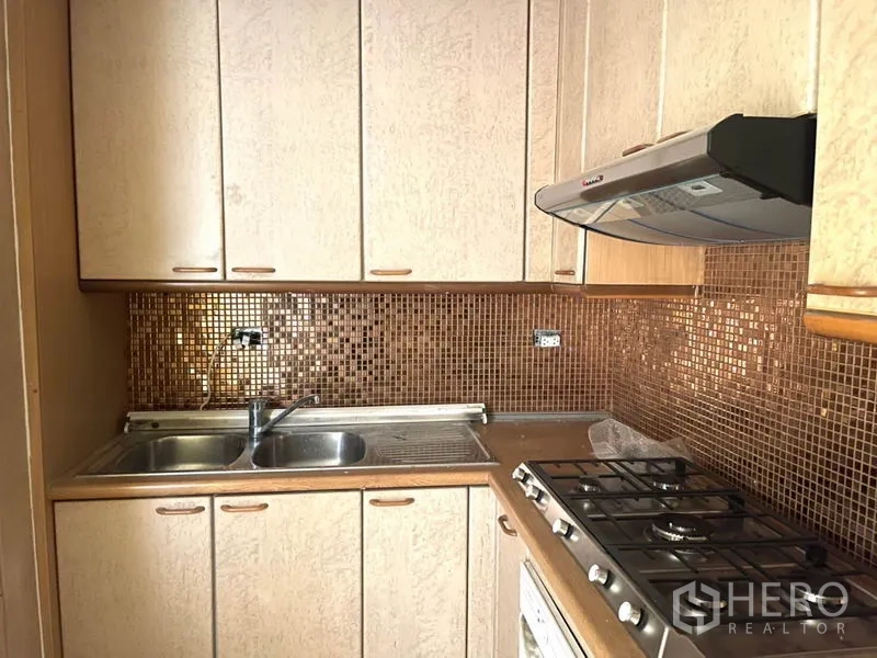 公寓 出租在Watthana, Bangkok - 紧凑厨房，燃气灶、抽油烟机、双槽水槽与马赛克墙面。