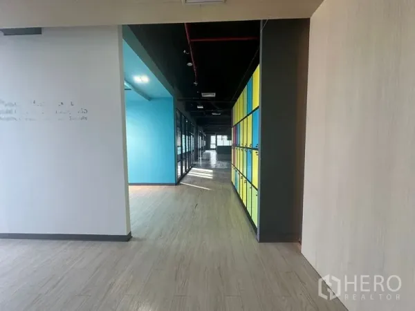 Office Space for rent in Bang Rak, Bangkok - Hallway of modern office with wood floors, exposed ceiling and colorful lockers leading to glass-partitioned rooms.