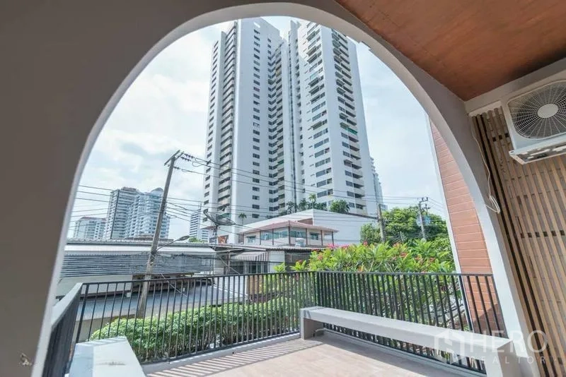Townhouse for rent in Watthana, Bangkok - Covered terrace with arched opening and city high-rise view beyond black railing.
