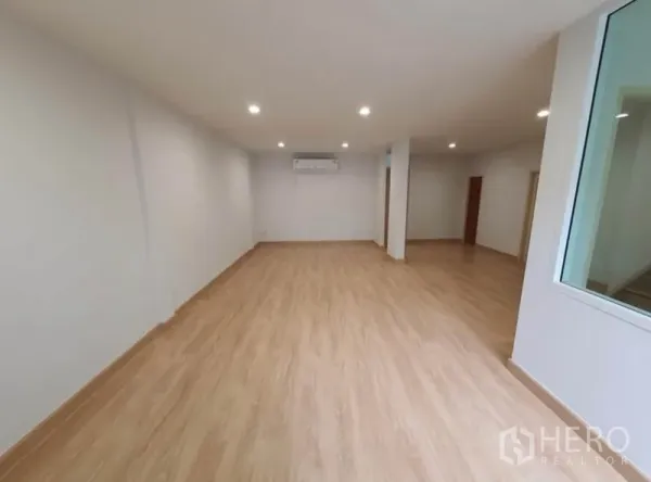 Townhouse for rent in Phaya Thai, Bangkok - Long open room with wood laminate floors, downlights and wall-mounted air conditioner.