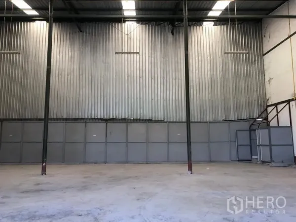 Warehouse for rent in Lat Krabang, Bangkok - Open warehouse space with tall steel columns, metal-clad wall, mezzanine stairs and overhead lighting.