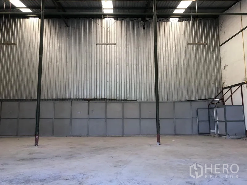 Warehouse for rent in Lat Krabang, Bangkok - Open warehouse space with tall steel columns, metal-clad wall, mezzanine stairs and overhead lighting.