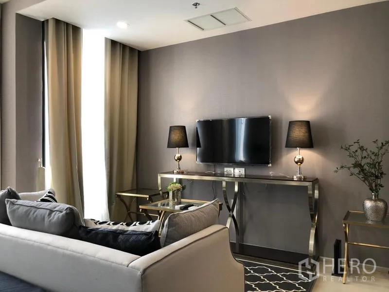 Condominium for rent in Pathum Wan, Bangkok - Elegant living area with wall-mounted TV, mirrored console and twin lamps at Noble Ploenchit condo.