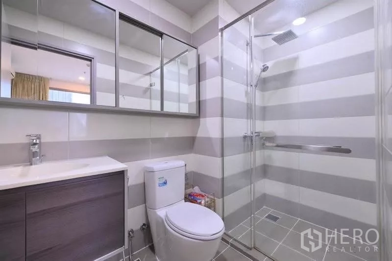Condominium for rent in Watthana, Bangkok - Contemporary bathroom with striped tiles, vanity and glass‑enclosed rain shower.