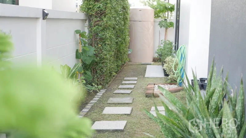 Detached House for rent or sale in Bang Bo, Samut Prakan - Side yard with stepping-stone walkway, hedge and outdoor water tank.