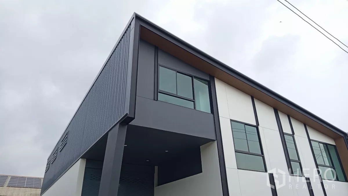 货栈 出租或出售在Lam Luk Ka, Pathum Thani - 建筑转角特写，金属包板、雨棚和二层办公室窗户。