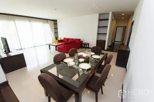 Apartment for rent in Sathon, Bangkok - Dining area with glass table for six facing a bright lounge and full-height curtains.