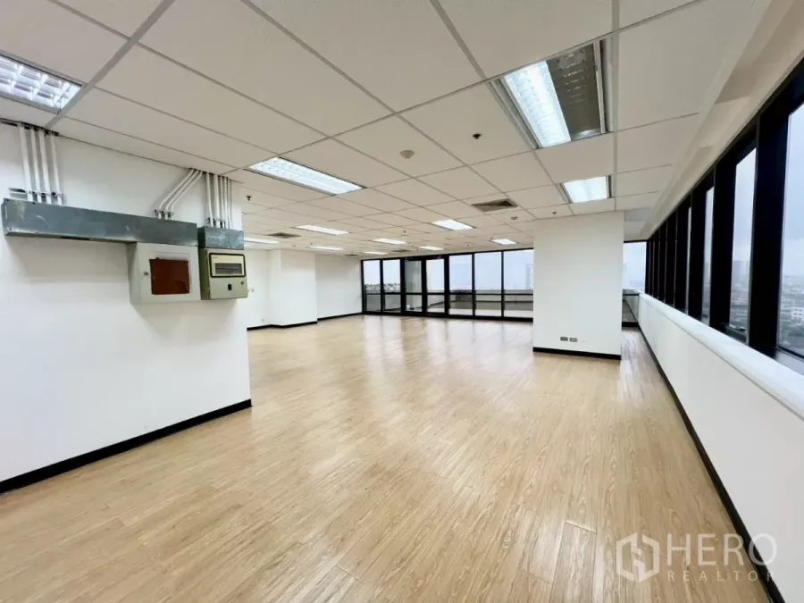 Office Space for rent in Huai Khwang, Bangkok - Corner office interior with wood-look floors, drop ceiling lighting, wall-mounted electrical panels and wide windows.