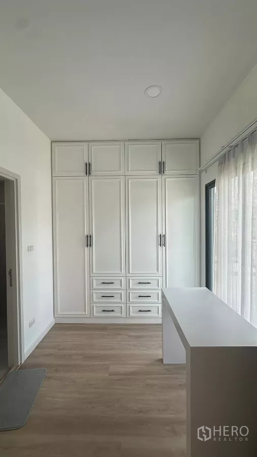 บ้าน ให้เช่าหรือขายในKhlong Toei, Bangkok - มุมห้องนอนพร้อมตู้เสื้อผ้าบานสูงจรดเพดาน และโต๊ะทำงานข้างผ้าม่านโปร่ง.