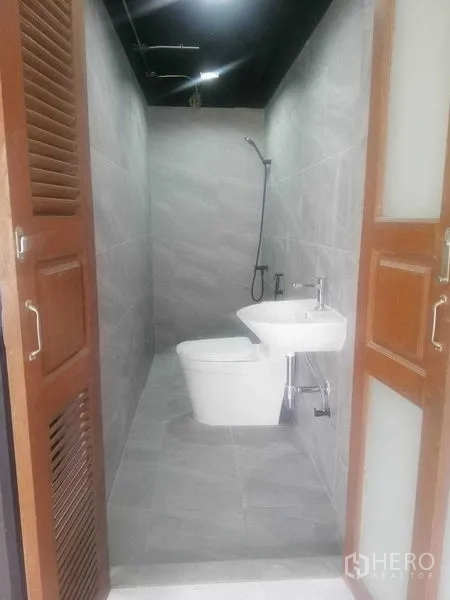 Shophouse for rent in Khlong Toei, Bangkok - Modern gray-tiled bathroom with toilet, sink and shower.