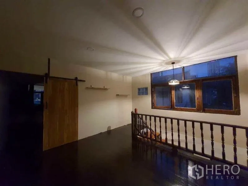 Detached House for rent in Pathum Wan, Bangkok - Upper-floor landing with pendant lighting, wooden railing and barn-style sliding door at night