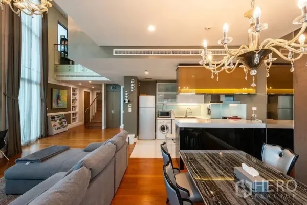 คอนโด ให้เช่าในKhlong Toei, Bangkok - ห้องนั่งเล่นและรับประทานอาหารเพดานสูง โซฟาสีเทา โคมระย้า และครัวแบบเปิด