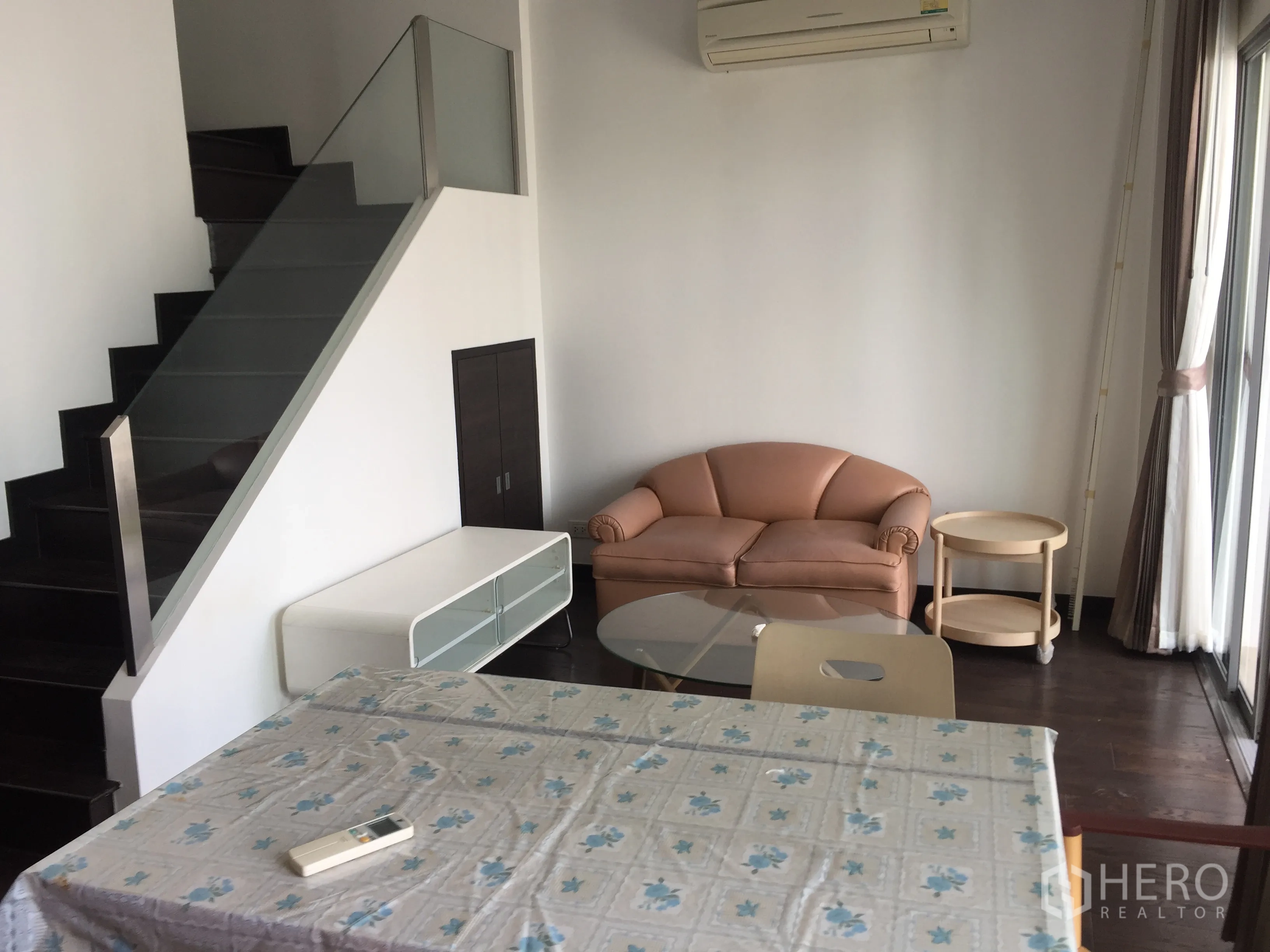 Condominium for rent in Ratchathewi, Bangkok - Loft-style living area with sofa, glass coffee table and staircase with glass railing.