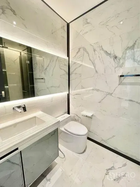 Condominium for rent in Watthana, Bangkok - Luxury bathroom with marble walls, backlit vanity, wall-mounted faucet and modern toilet.