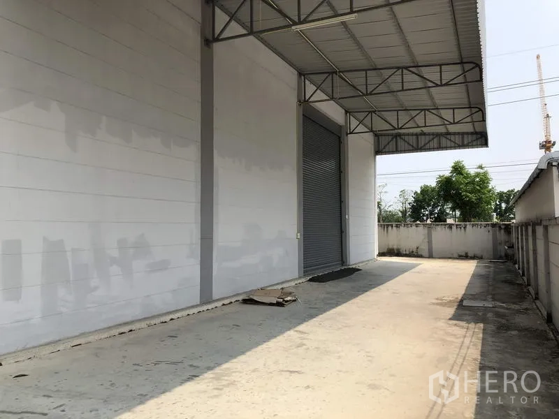 โรงงาน ให้เช่าในLam Luk Ka, Pathum Thani - ลานขนถ่ายสินค้ามีชายคาเมทัลชีท ประตูม้วน และพื้นคอนกรีตกว้างข้างกำแพงรั้ว