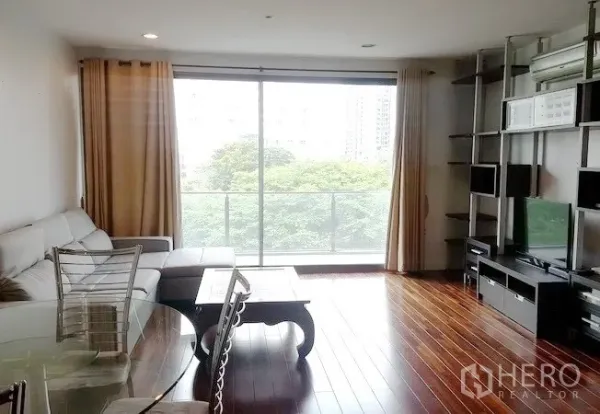 คอนโด ให้เช่าในKhlong Toei, Bangkok - ห้องนั่งเล่นโอเพ่นแปลน ประตูบานเลื่อนกระจกเต็มผนังออกสู่ระเบียง ชั้นวางทีวีบิวท์อินและโซฟามุม มองเห็นวิวต้นไม้