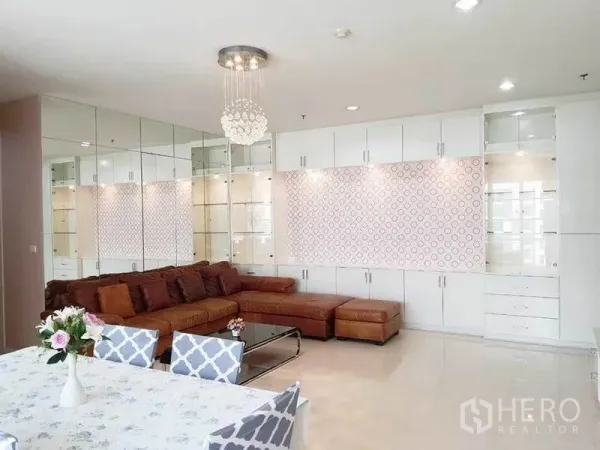 公寓 出租在Ratchathewi, Bangkok - 客厅设棕色L型真皮沙发、水晶吊灯与镜面储物柜。