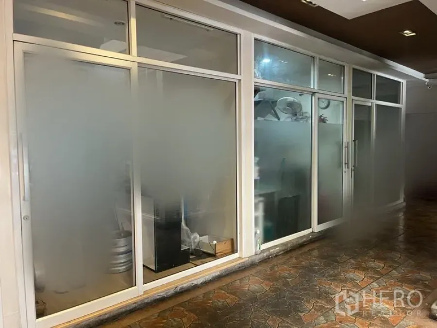 零售空间 出租在Khlong Toei, Bangkok - 磨砂玻璃店面，白色铝合金框架与推拉门，临有顶棚的石纹走道。