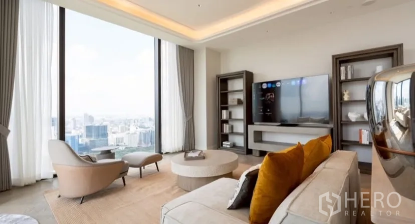 公寓 出租或出售在Pathum Wan, Bangkok - 明亮客厅，电视墙与书架、舒适沙发，面向落地窗城市景色。