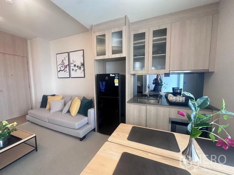 คอนโด ให้เช่า - ครัวบิลท์อินโทนไม้ เคาน์เตอร์สีดำ ตู้เย็น และโซฟาในพื้นที่นั่งเล่น