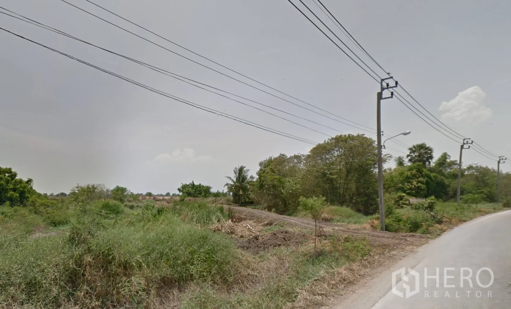 Land for sale in Bang Bo, Samut Prakan - Roadside view of vacant land in Bang Bo, Samut Prakan with utility poles and overhead power lines.