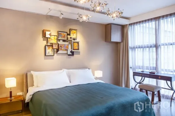 公寓 出租在Watthana, Bangkok - 舒适卧室，特大床、装饰画与枝形吊灯，落地窗旁设有书桌。