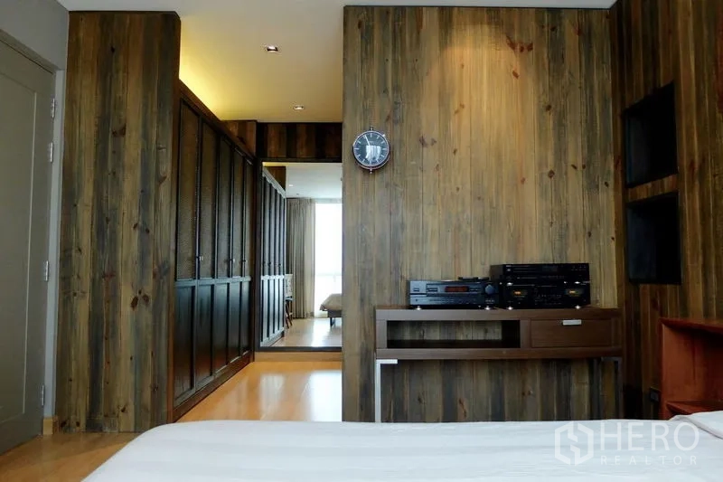 Condominium for sale in Watthana, Bangkok - Bedroom view toward the hallway with wood cladding and a storage console.