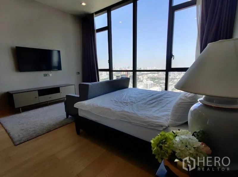 Condominium for rent in Watthana, Bangkok - Guest bedroom angle showing wall-mounted TV, bed, and full-height windows with skyline view.
