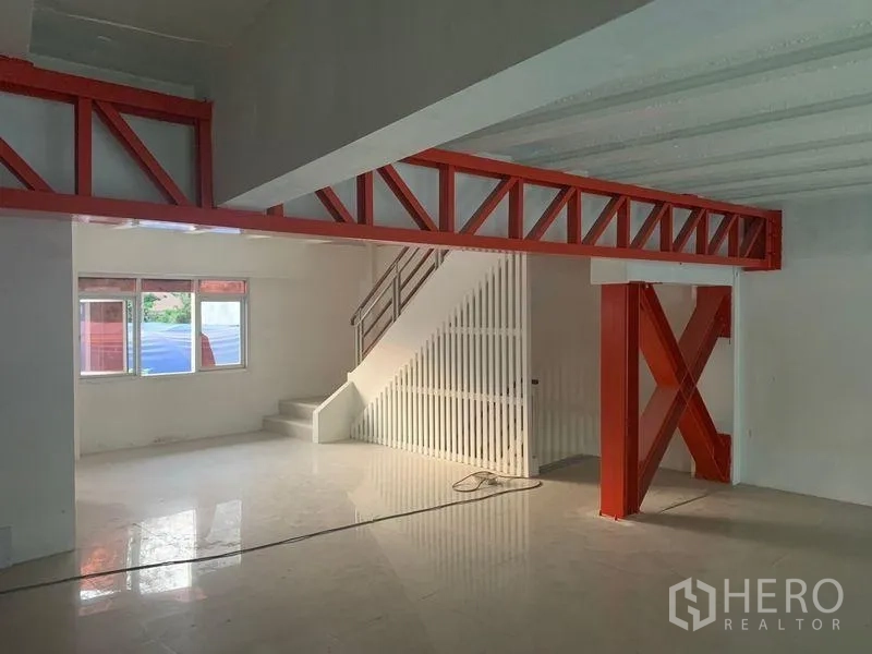 Shophouse for rent in Prawet, Bangkok - Open-plan floor with red steel beams, glossy tiles and an internal staircase.