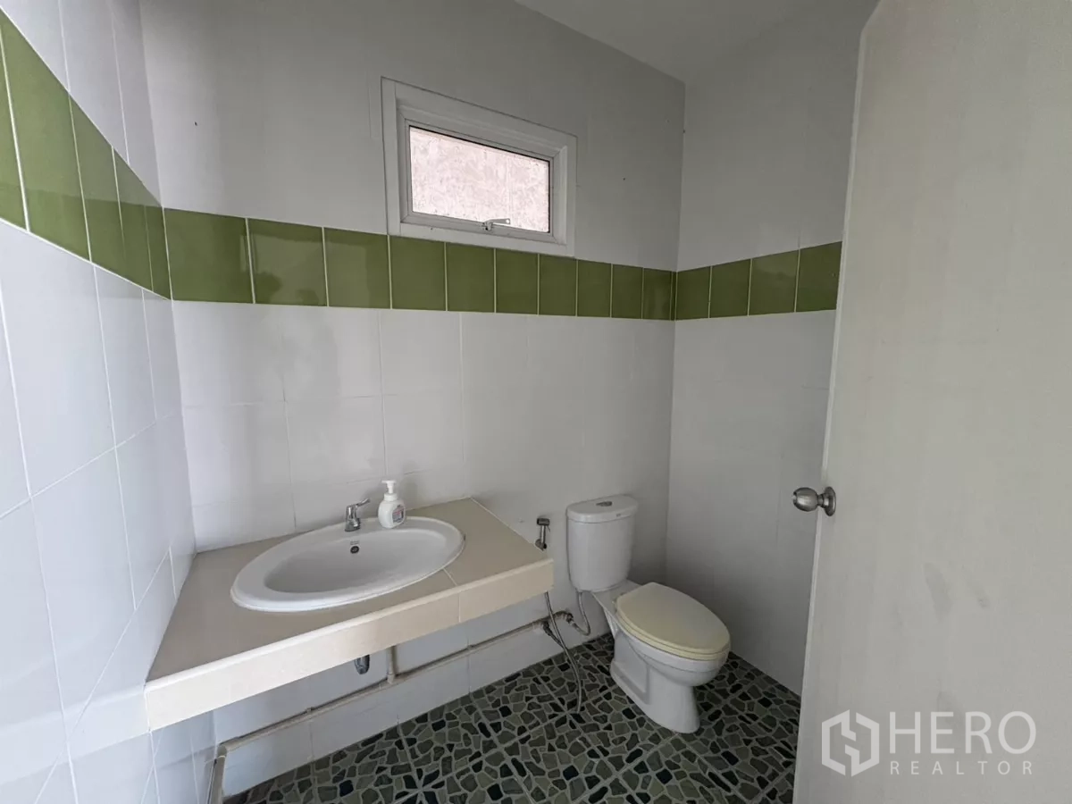 Warehouse for rent or sale in Bang Bo, Samut Prakan - Clean restroom with sink, toilet and green accent tiles.