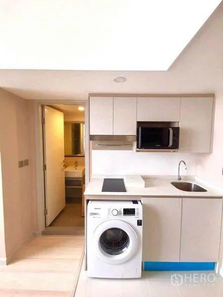 คอนโด ให้เช่าในSathon, Bangkok - ครัวบิวท์อินตู้สีขาว เตาไฟฟ้า ไมโครเวฟ อ่างล้างจาน และเครื่องซักผ้า โดยมีห้องน้ำถัดไป