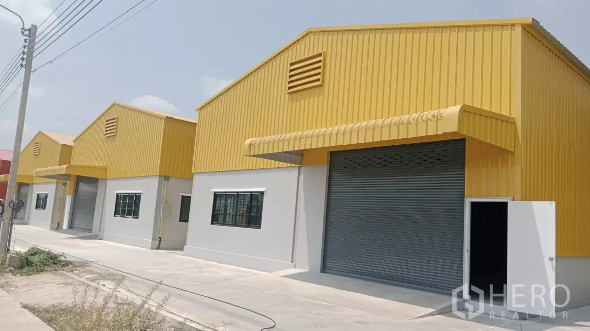 Warehouse for rent in Nonthaburi - Row of modern yellow-roof warehouses with large roller shutters and a wide concrete driveway in Pak Kret, Nonthaburi.
