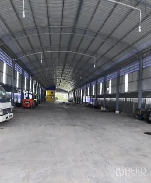 Warehouse for sale in Sai Noi, Nonthaburi - Long clear-span warehouse floor with trucks and a forklift under a high roof.