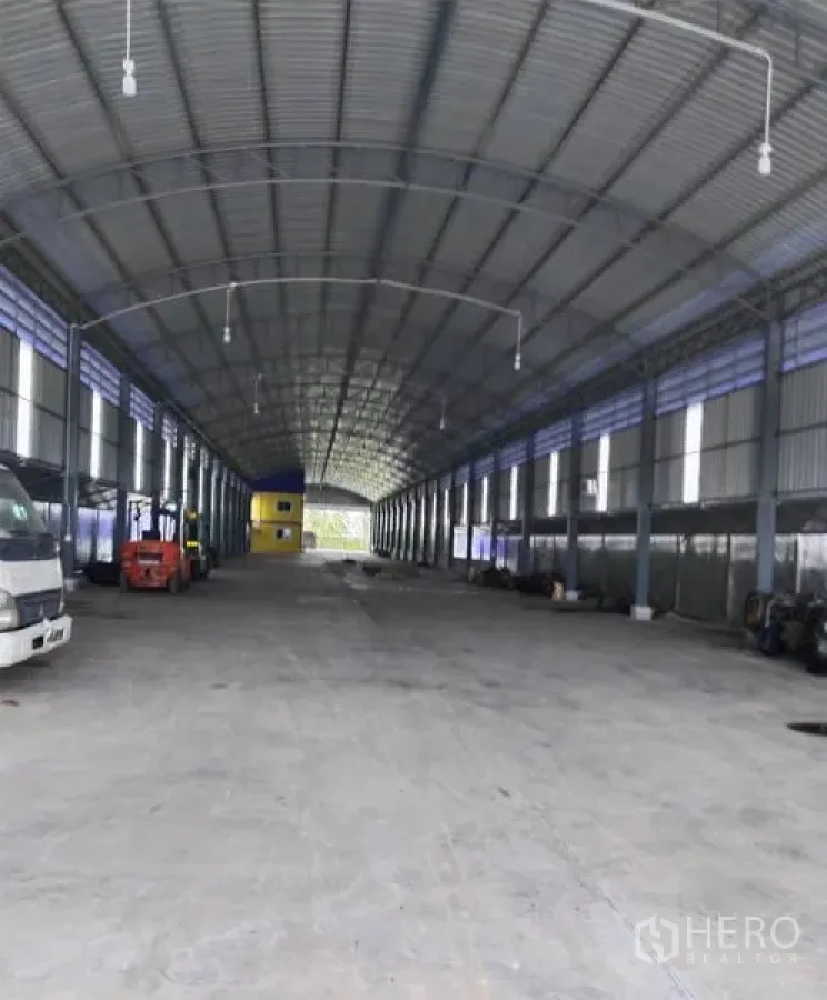 Warehouse for sale in Sai Noi, Nonthaburi - Long clear-span warehouse floor with trucks and a forklift under a high roof.