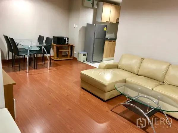 Condominium for rent in Huai Khwang, Bangkok - Dining corner beside the kitchen with a glass-top table and chairs on wood flooring.