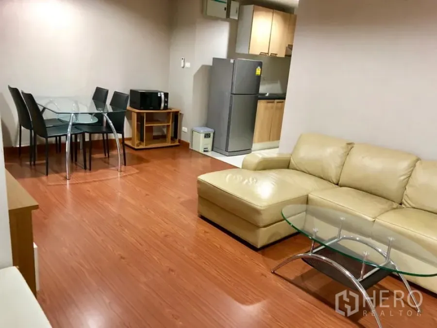 Condominium for rent in Huai Khwang, Bangkok - Dining corner beside the kitchen with a glass-top table and chairs on wood flooring.