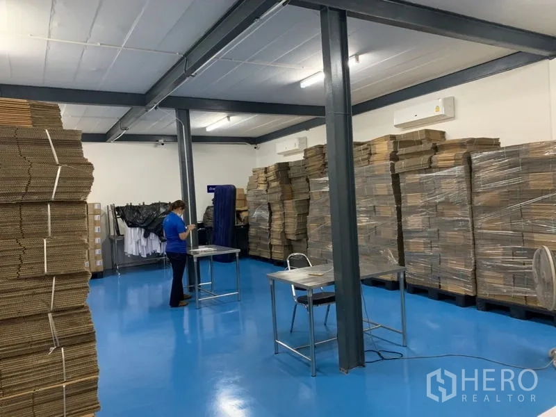 คลังสินค้า ให้เช่าในBang Kapi, Bangkok - โซนจัดเก็บกว้างพื้นสีน้ำเงิน กล่องวางบนพาเลท ไฟฟลูออเรสเซนต์ และโครงสร้างเหล็ก.