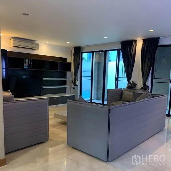 Detached House for rent in Din Daeng, Bangkok - Spacious living room with gray sofas, media wall and large windows.