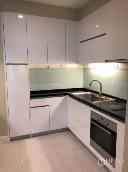 公寓 出租或出售在Khlong Toei, Bangkok - 现代白色L型厨房，内置烤箱、电磁炉与不锈钢水槽。