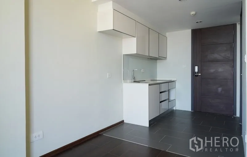 Condominium for sale in Watthana, Bangkok - Minimalist kitchenette with upper cabinets, sink and dark tile floor at the condo entry.