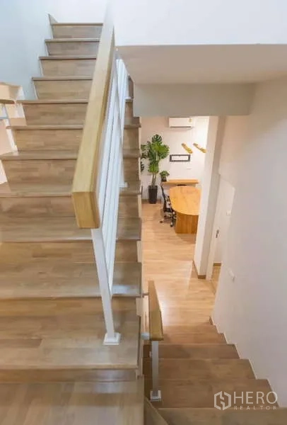 独立式住宅 出租或出售在Lat Phrao, Bangkok - 木质楼梯与白色扶手，俯瞰开放式起居空间。