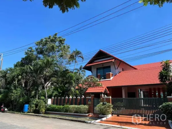 Detached House for rent in Bang Phli, Samut Prakan - Street view of a two-storey detached house with red tiled roof, brick exterior and gated fence amid greenery in Bang Phli.