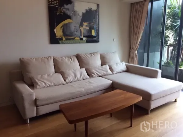 Condominium for rent in Sathon, Bangkok - Bright living room with L-shaped sofa, wood coffee table and floor-to-ceiling sliding doors to a green balcony.