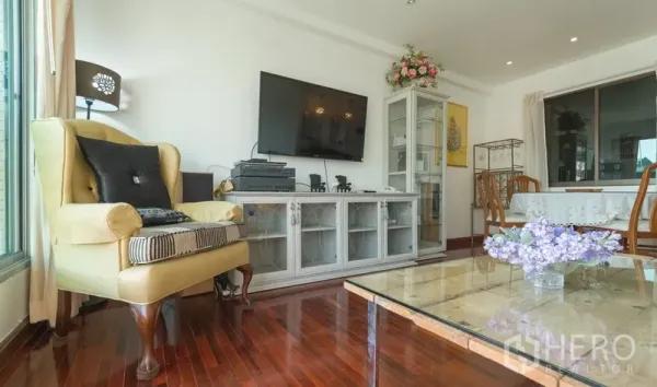Condominium for rent in Pathum Wan, Bangkok - Lounge area with armchair, wall-mounted TV and display cabinet beside a glass-top table.