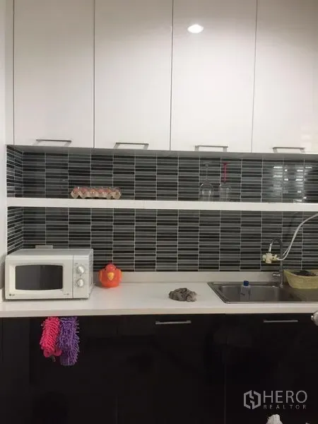 联排别墅 出租或出售在Wang Thonglang, Bangkok - 现代厨房，白色橱柜与黑色条纹瓷砖背景墙，配水槽和微波炉。