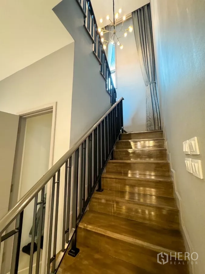 Detached House for rent or sale in Bueng Kum, Bangkok - Staircase with black metal railing and contemporary chandelier.