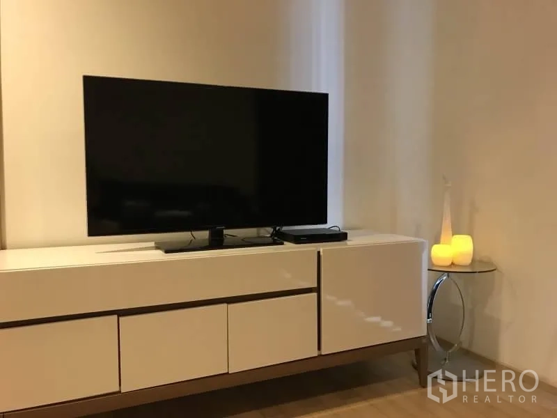 คอนโด ให้เช่าในKhlong Toei, Bangkok - มุมนั่งเล่นสไตล์มินิมอล ทีวีจอแบนวางบนตู้วางทีวีสีขาว พร้อมแสงไฟอบอุ่น