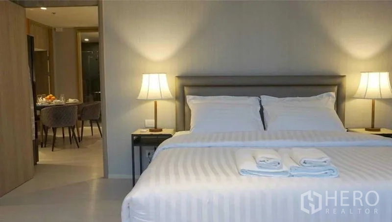 Condominium for rent in Pathum Wan, Bangkok - Master bedroom with king bed, matching bedside lamps and a view into the dining area.