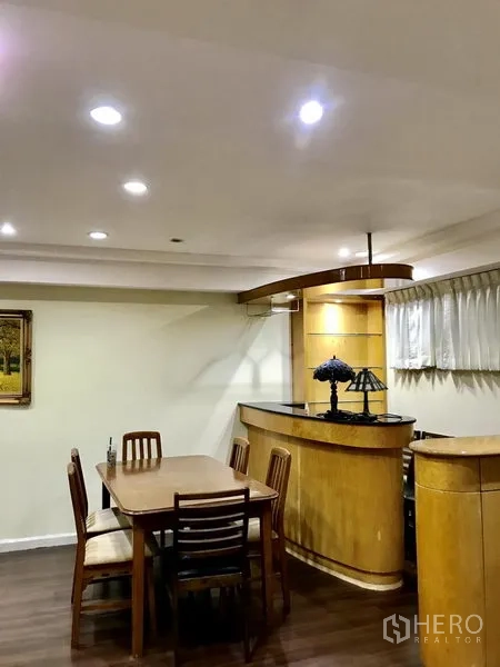 Condominium for rent in Watthana, Bangkok - Dining area with wooden table and chairs beside the bar under recessed ceiling lights.