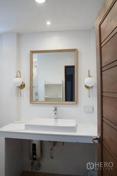Detached House for rent in Wang Thonglang, Bangkok - Vanity with square mirror and wall sconces in a clean white bathroom.
